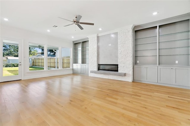 unfurnished living room featuring crown molding, ceiling fan, a fireplace, light hardwood / wood-style floors, and built in shelves