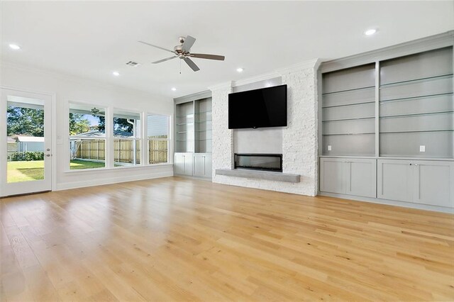 unfurnished living room featuring a fireplace, built in shelves, light wood-type flooring, and crown molding