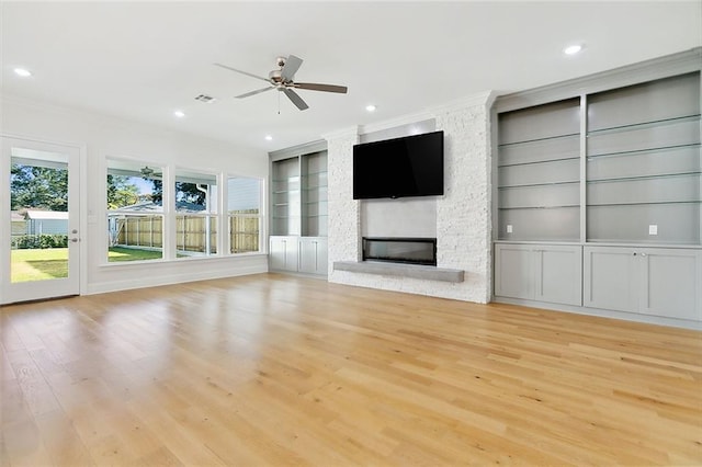 unfurnished living room featuring built in shelves, a fireplace, ornamental molding, and light wood-type flooring