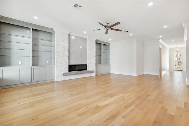 unfurnished living room featuring built in features, a stone fireplace, crown molding, and light hardwood / wood-style floors