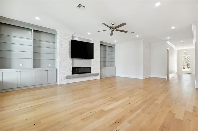 unfurnished living room with crown molding, a fireplace, built in features, and light hardwood / wood-style floors