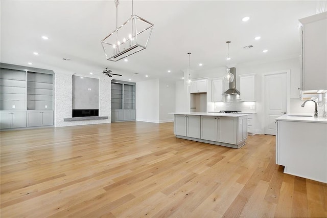 kitchen featuring light wood-type flooring, a fireplace, a kitchen island, and wall chimney exhaust hood