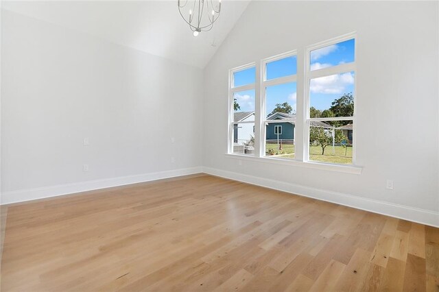 spare room with a notable chandelier, high vaulted ceiling, and light hardwood / wood-style floors