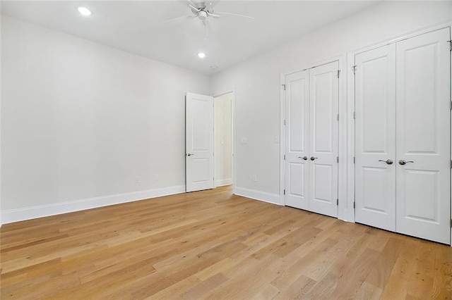 unfurnished bedroom featuring ceiling fan, multiple closets, and light wood-type flooring