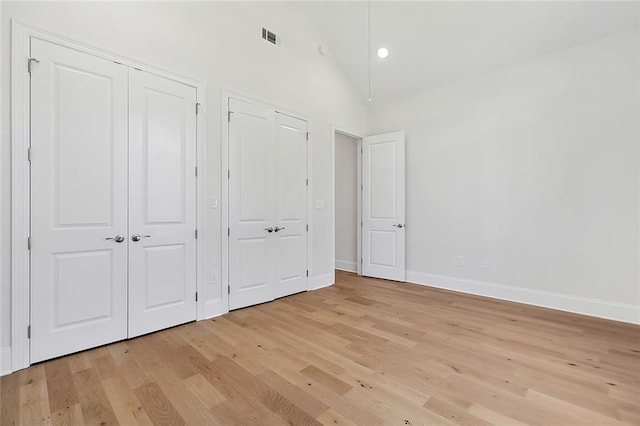 unfurnished bedroom featuring high vaulted ceiling, multiple closets, and light wood-type flooring