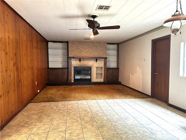 unfurnished living room with brick wall, a fireplace, light tile patterned floors, wood walls, and ceiling fan