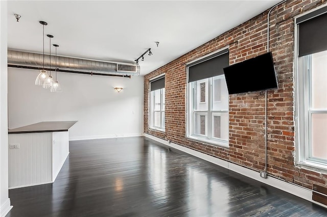 unfurnished living room featuring brick wall, rail lighting, and dark hardwood / wood-style floors