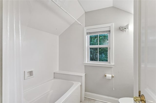 bathroom featuring tile patterned floors, vaulted ceiling, a tub to relax in, and toilet