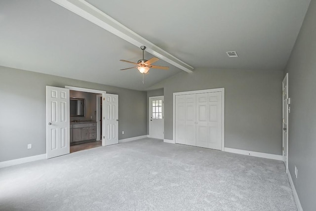 unfurnished bedroom with ensuite bathroom, carpet floors, ceiling fan, vaulted ceiling with beams, and a closet