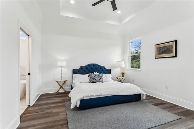 bedroom with dark wood-type flooring, a tray ceiling, ensuite bathroom, and ceiling fan