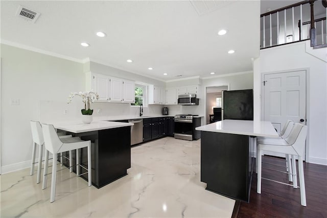 kitchen featuring a kitchen bar, appliances with stainless steel finishes, white cabinetry, and sink