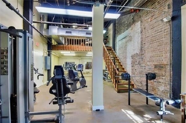 workout area with a high ceiling, brick wall, and concrete floors