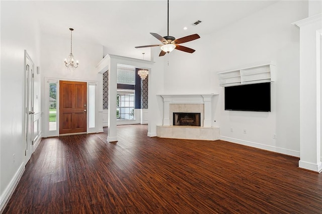 unfurnished living room with a tile fireplace, a high ceiling, ceiling fan with notable chandelier, and dark hardwood / wood-style flooring