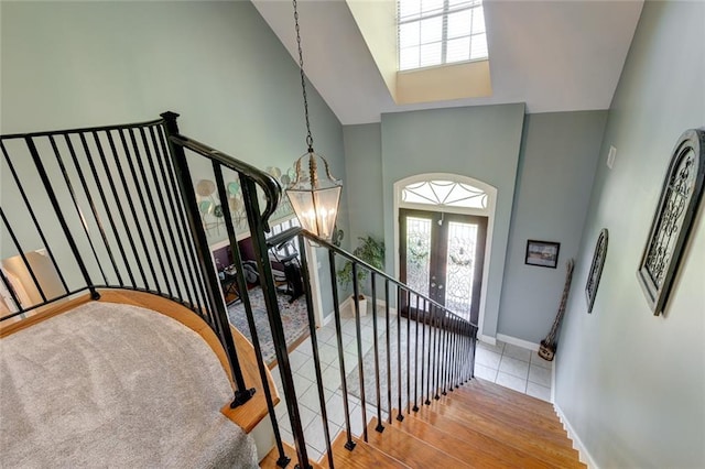 stairs featuring french doors, hardwood / wood-style flooring, a towering ceiling, and a chandelier