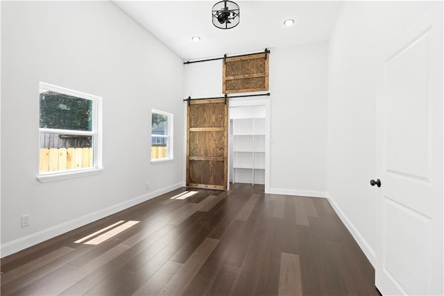 unfurnished bedroom featuring dark wood-type flooring, a walk in closet, and a barn door