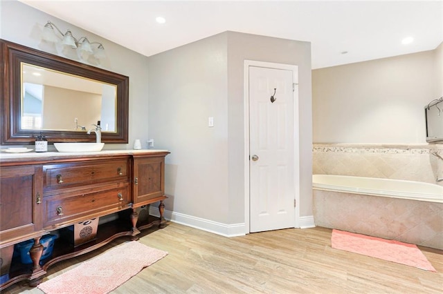 bathroom with tiled tub, vanity, and hardwood / wood-style flooring