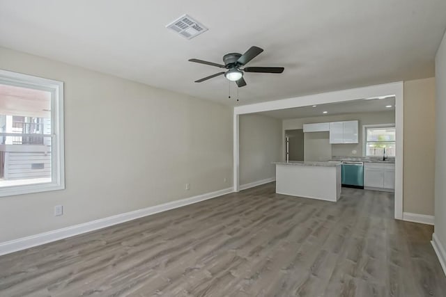 unfurnished living room with visible vents, a ceiling fan, a sink, wood finished floors, and baseboards