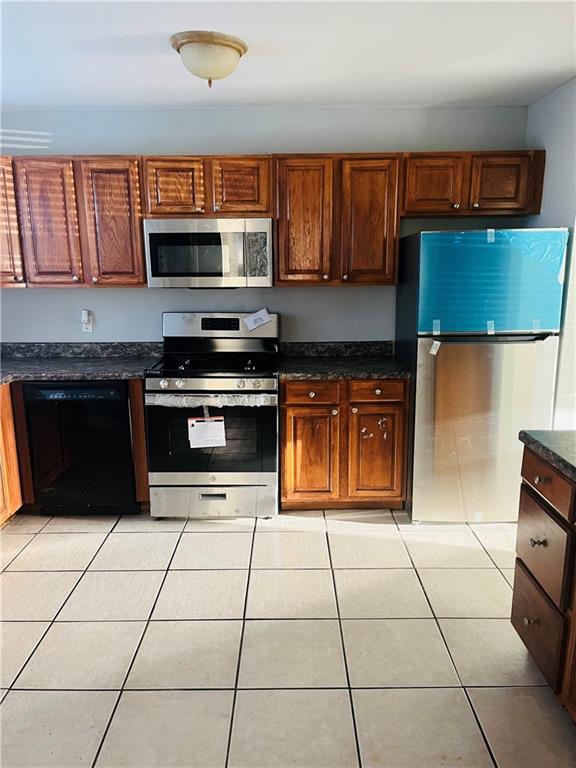 kitchen with light tile patterned flooring, stainless steel appliances, and dark stone counters