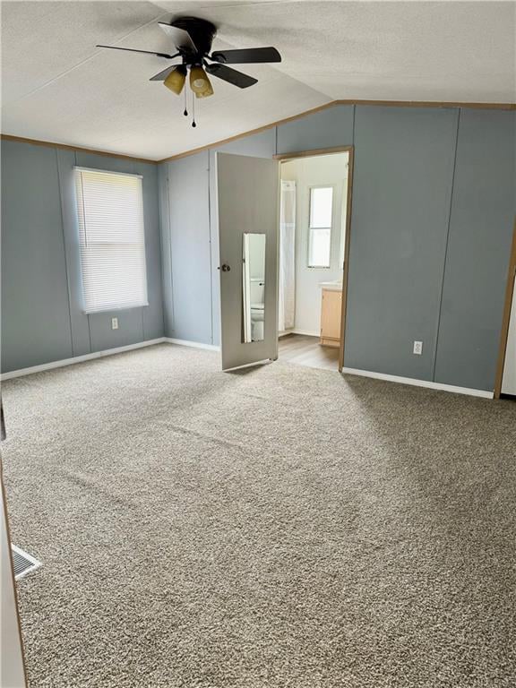 unfurnished bedroom with a textured ceiling, connected bathroom, ceiling fan, light carpet, and vaulted ceiling