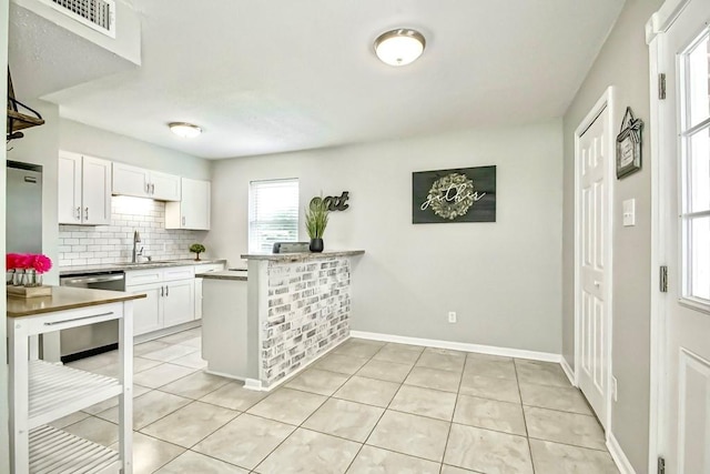 kitchen featuring white cabinetry, light tile patterned floors, stainless steel dishwasher, decorative backsplash, and sink