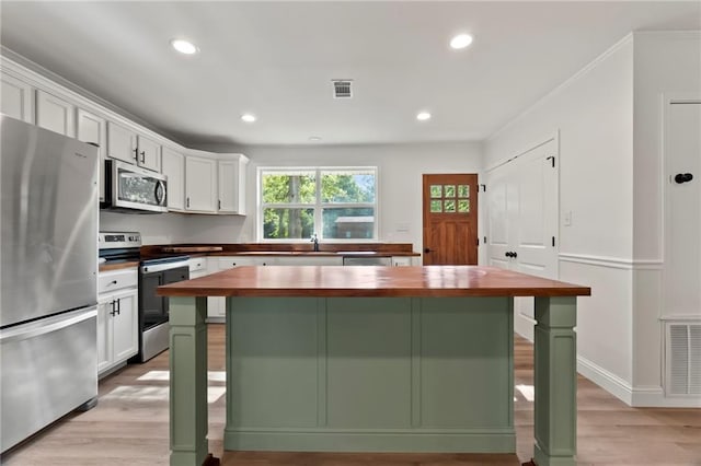 kitchen featuring a kitchen island, appliances with stainless steel finishes, a breakfast bar, butcher block countertops, and white cabinets