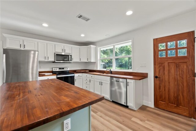 kitchen with white cabinets, stainless steel appliances, butcher block countertops, and light wood-type flooring