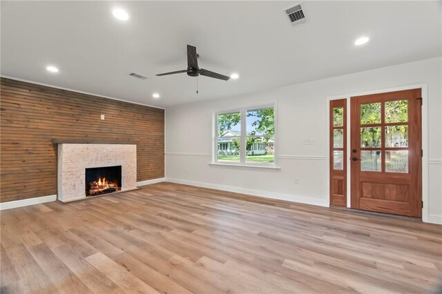 unfurnished living room featuring light hardwood / wood-style floors, a stone fireplace, wood walls, and ceiling fan