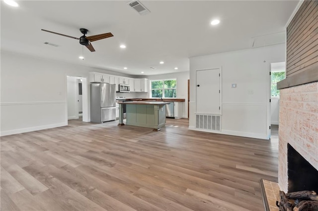 unfurnished living room with a stone fireplace, light hardwood / wood-style flooring, and ceiling fan