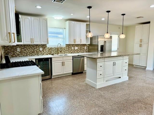 kitchen with sink, light stone counters, a kitchen island, stainless steel appliances, and white cabinets