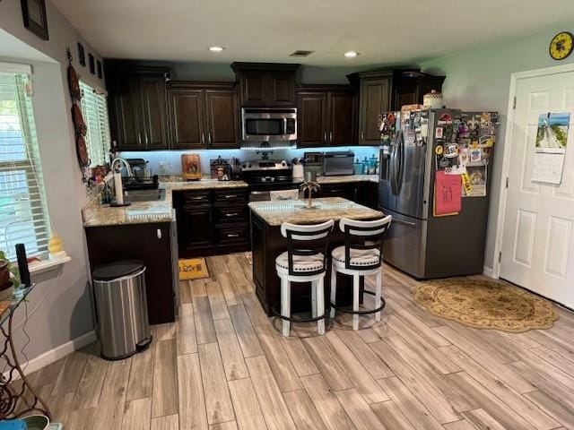 kitchen with appliances with stainless steel finishes, light wood-type flooring, light stone counters, dark brown cabinetry, and sink