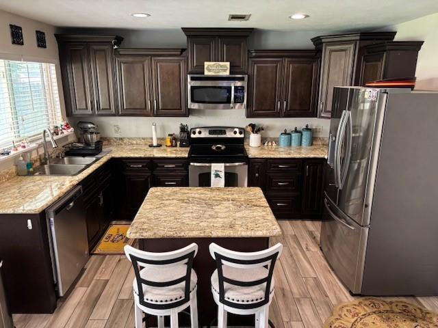 kitchen with a breakfast bar, sink, light hardwood / wood-style floors, and appliances with stainless steel finishes