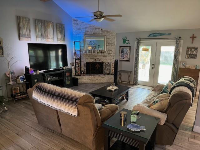 living room with ceiling fan, french doors, a brick fireplace, light hardwood / wood-style floors, and vaulted ceiling