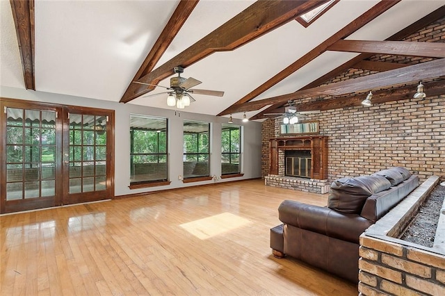 living room featuring vaulted ceiling with beams, a fireplace, brick wall, and light hardwood / wood-style flooring