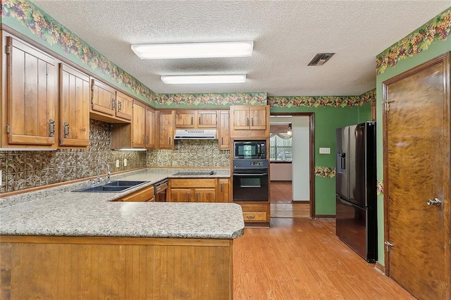 kitchen featuring black appliances, sink, light hardwood / wood-style floors, a textured ceiling, and kitchen peninsula