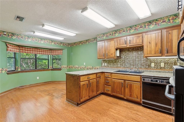 kitchen featuring black dishwasher, tasteful backsplash, sink, kitchen peninsula, and light wood-type flooring