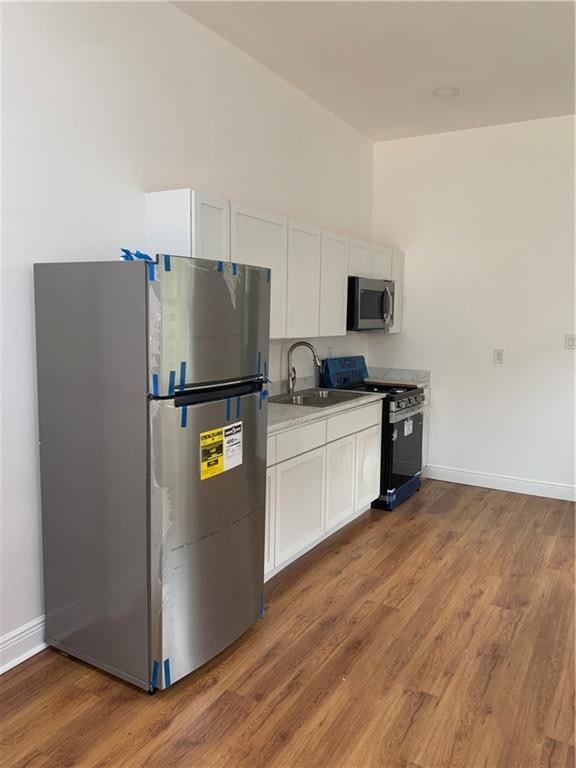 kitchen with appliances with stainless steel finishes, sink, wood-type flooring, and white cabinetry