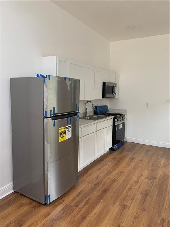 kitchen with white cabinetry, wood finished floors, a sink, and stainless steel appliances