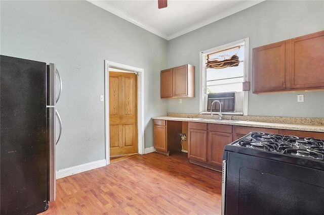 kitchen with light wood-type flooring, black gas range, ornamental molding, a sink, and freestanding refrigerator
