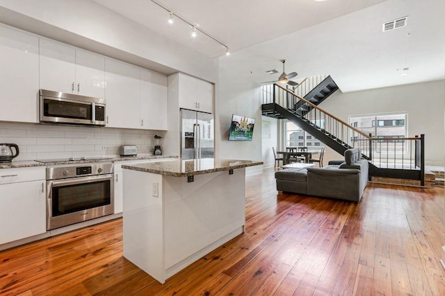 kitchen with appliances with stainless steel finishes, wood-type flooring, a kitchen island, and white cabinets