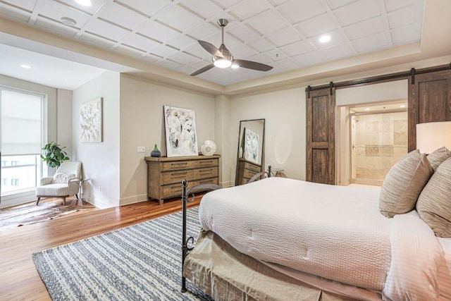 bedroom with wood-type flooring, ensuite bath, ceiling fan, and a barn door