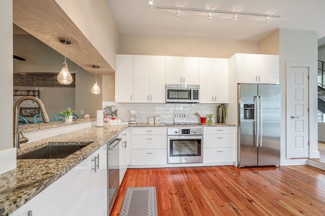 kitchen with hanging light fixtures, light hardwood / wood-style floors, white cabinetry, stainless steel appliances, and sink