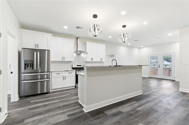 kitchen featuring appliances with stainless steel finishes, an island with sink, white cabinetry, dark wood-type flooring, and wall chimney exhaust hood