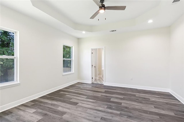 empty room with ceiling fan, a tray ceiling, and wood-type flooring