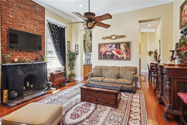 living room featuring ornamental molding, wood-type flooring, a brick fireplace, and ceiling fan