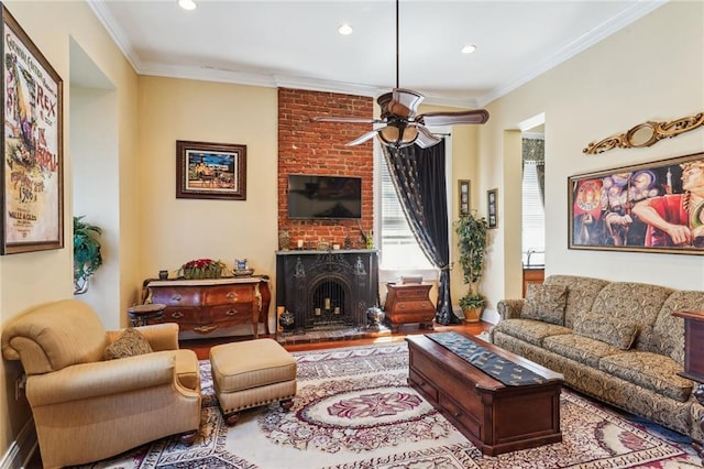 living room featuring wood-type flooring, a fireplace, ceiling fan, crown molding, and brick wall