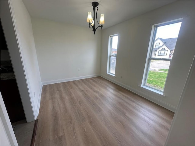 unfurnished room featuring a healthy amount of sunlight, an inviting chandelier, and light hardwood / wood-style floors