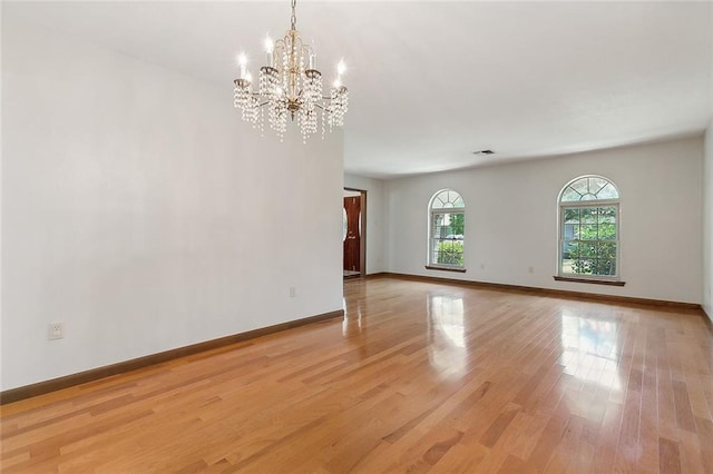 spare room with a notable chandelier and light wood-type flooring