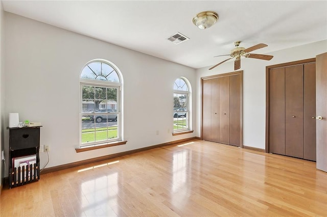 unfurnished bedroom with ceiling fan, multiple closets, light hardwood / wood-style floors, and multiple windows