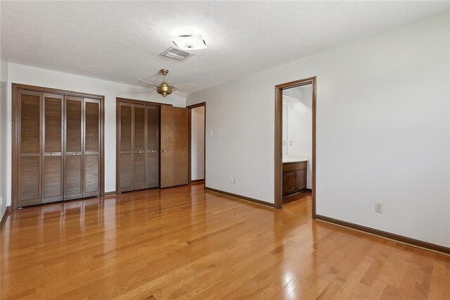 unfurnished bedroom with light wood-type flooring, ensuite bath, and two closets