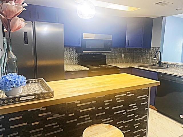 kitchen with tasteful backsplash, light tile patterned floors, black appliances, butcher block countertops, and sink